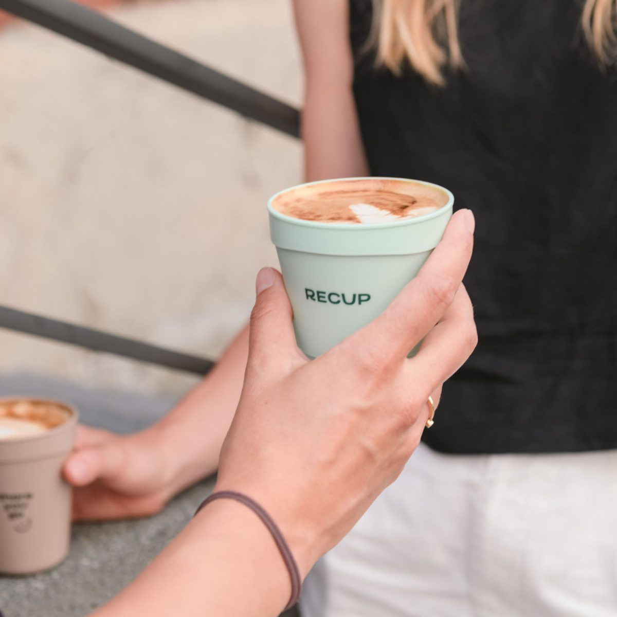 RECUP Pfandbecher wird mit Kaffee in der Hand gehalten.